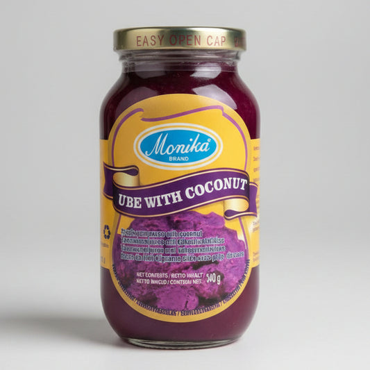 A glass jar of Monika Brand Ube with Coconut, featuring a yellow label with purple and brown accents, a gold metal lid, and the product filling most of the frame against a plain off-white background.